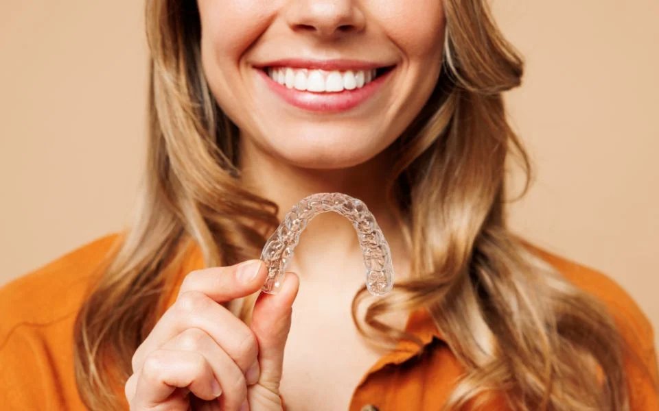 A patient smiling and holding her clear aligner tray.